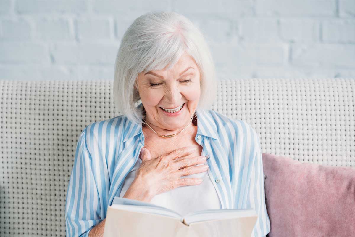 discovery-commons-cypress-point-feature-2-senior-woman-sitting-on-couch-smiling-reading-book