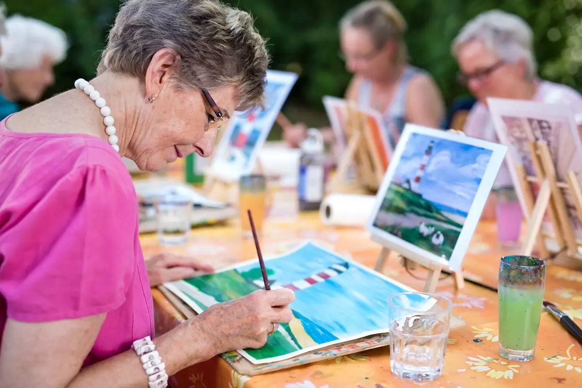 discovery commons cypress point feature 4 group of seniors painting pictures at long table outside