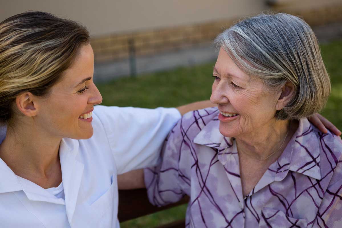 discovery-commons-cypress-point-feature-5-nurse-sitting-on-bench-with-arm-around-senior-woman's-shoulder-smiling