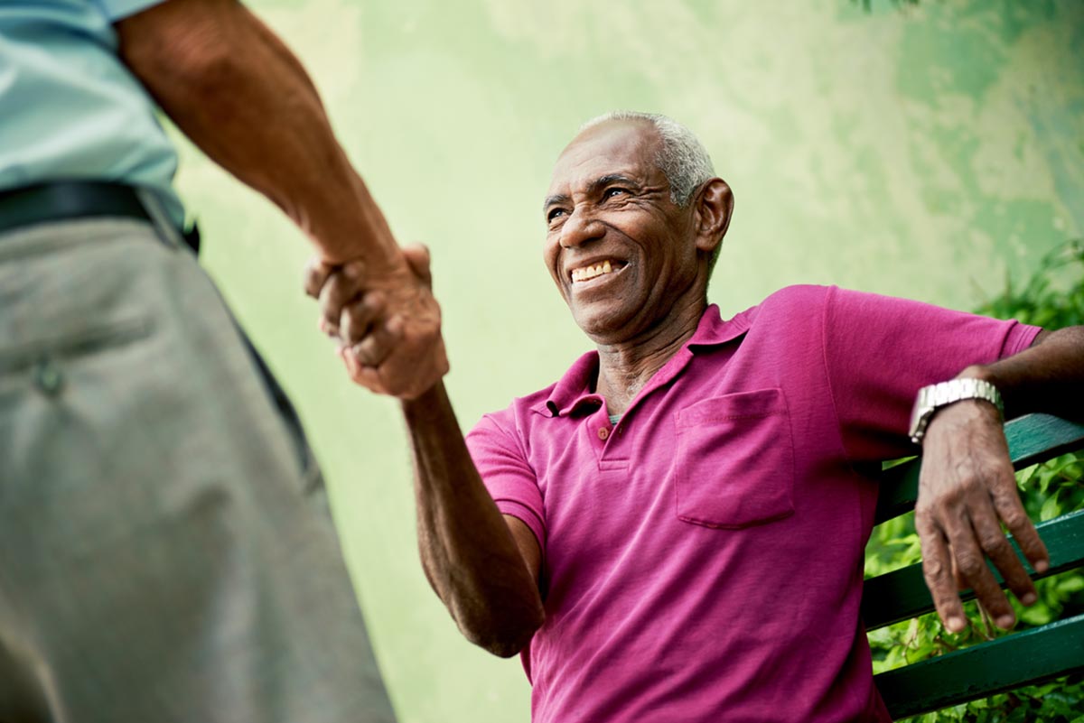 discovery commons cypress point feature 6 senior man sitting on bench smiling shaking hands with standing senior man